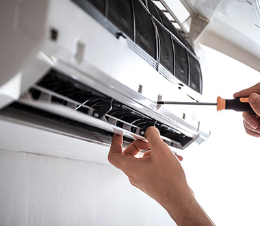 a person using an orange and black screwdriver to unscrew a split system air conditioner